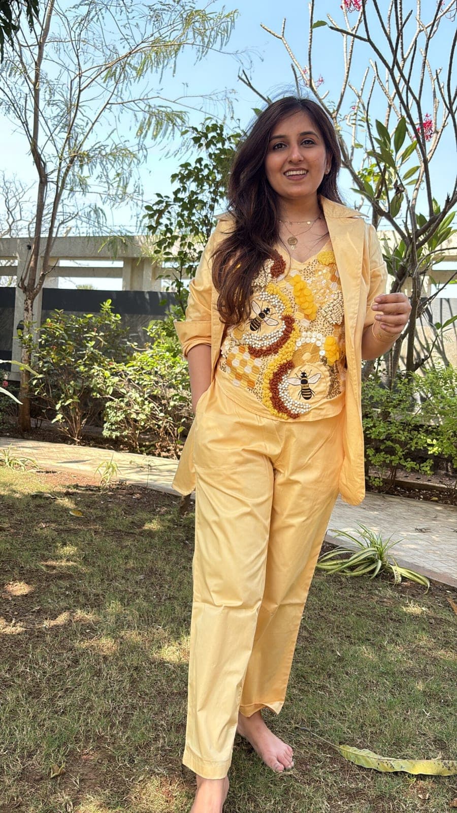 The same yellow set worn with full-length trousers, blazer sleeves rolled back, honeycomb beadwork covering the front of the top.