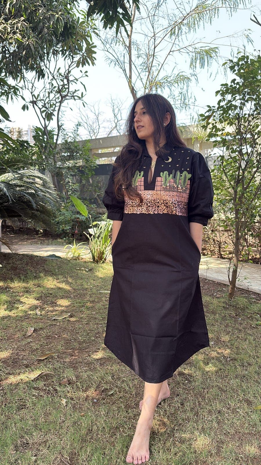 Hands in the side-seam pockets, the dress seen full length: collar, puffed three-quarter sleeves, black A-line falling to mid-calf.
