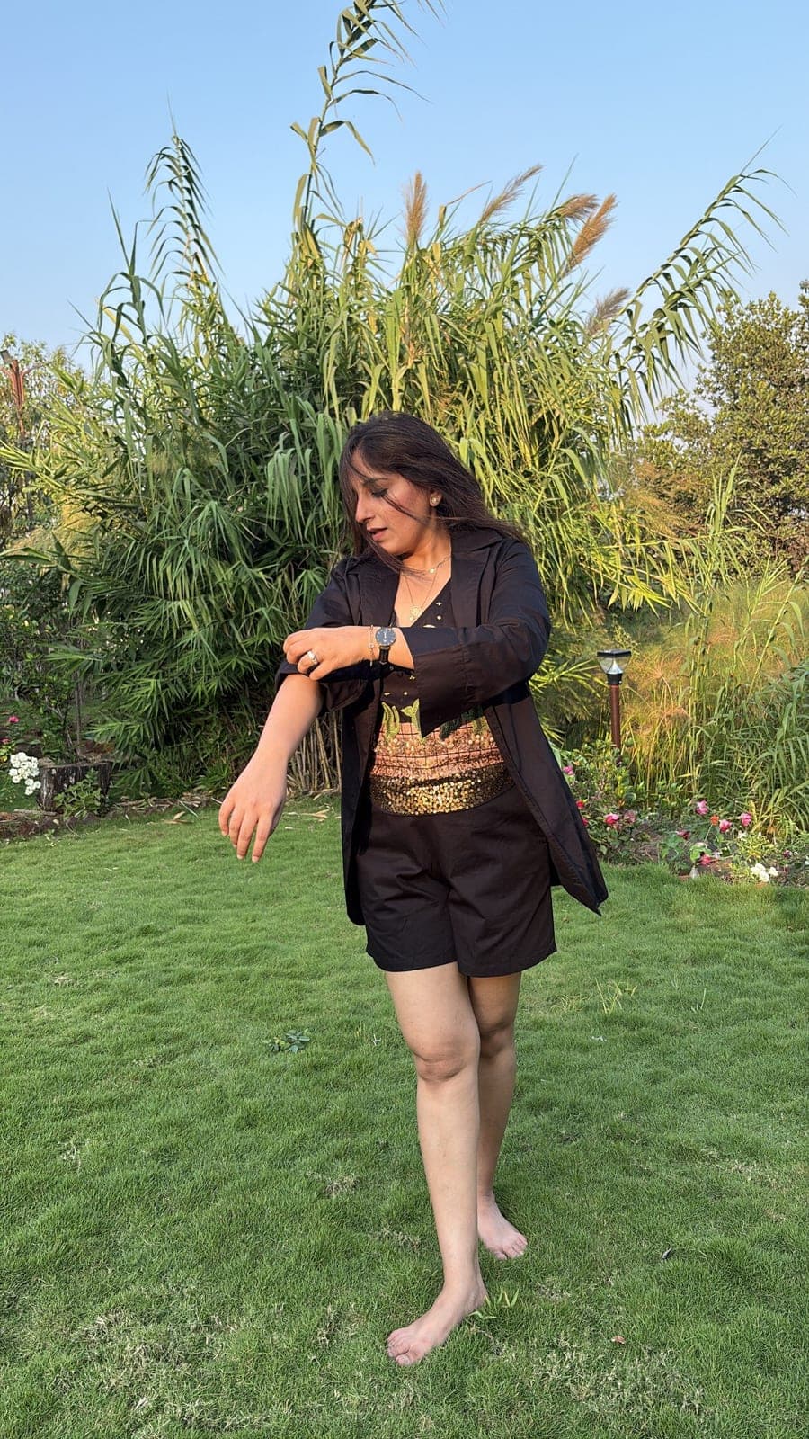Black cotton blazer worn open over the embroidered sleeveless top and matching shorts, standing on grass in late evening light.