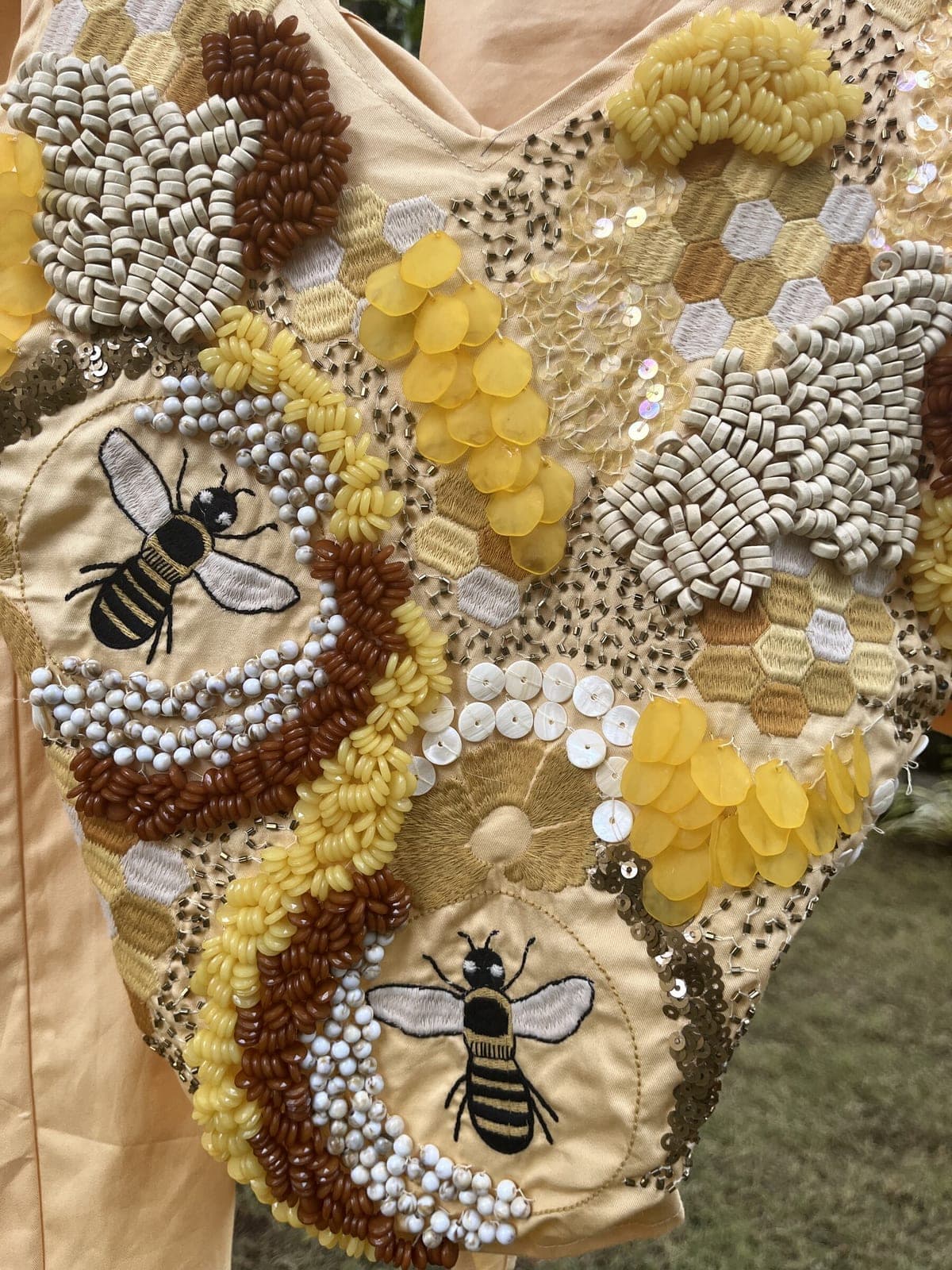 Close-up of the hand embroidery: two striped bees among pearl clusters, shell discs, yellow sequins and honeycomb cells in fine thread.