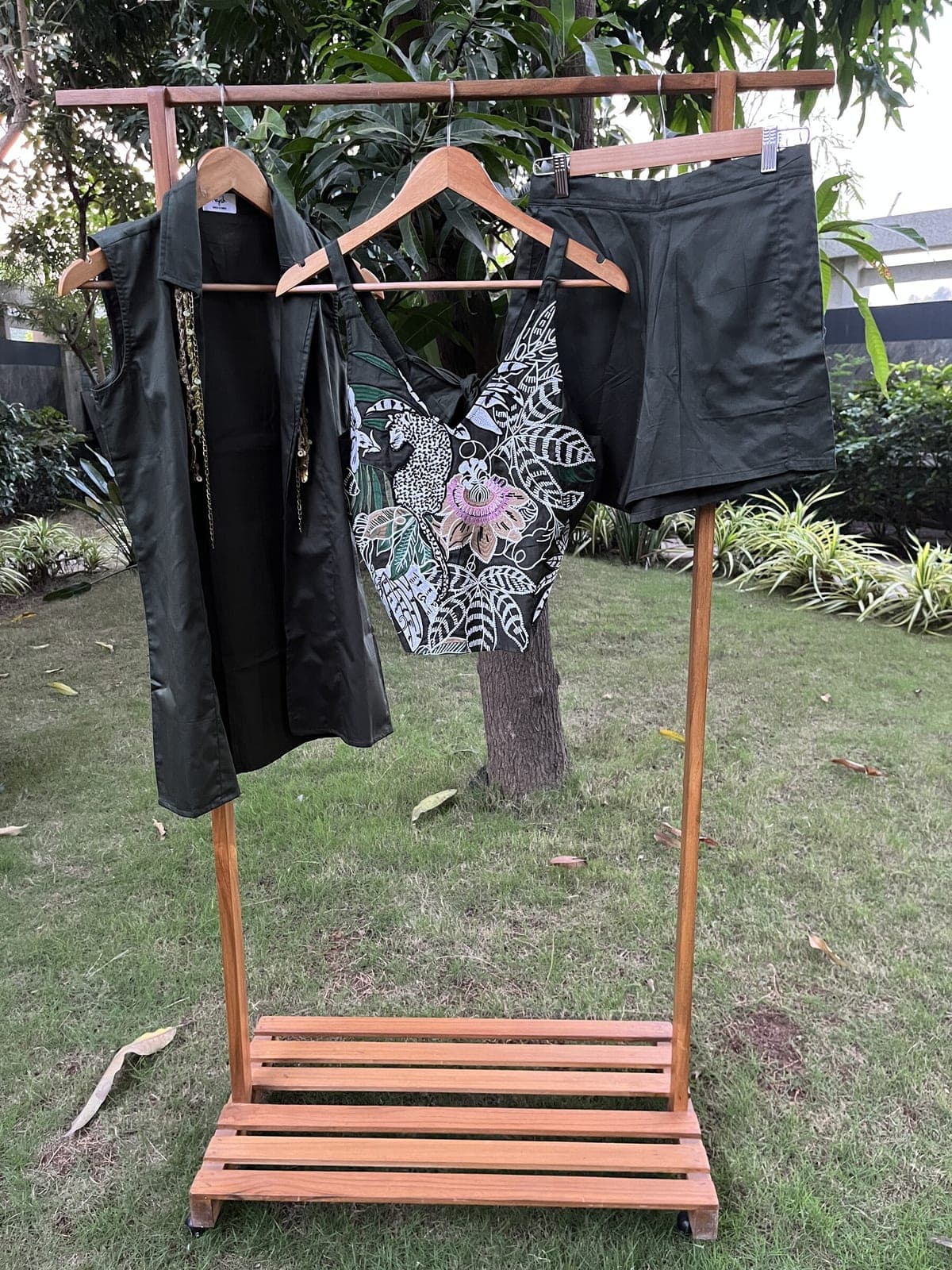 Dark green three-piece hung outdoors — long sleeveless blazer with beaded chains at the shoulder, heavily embroidered strappy top, plain shorts.