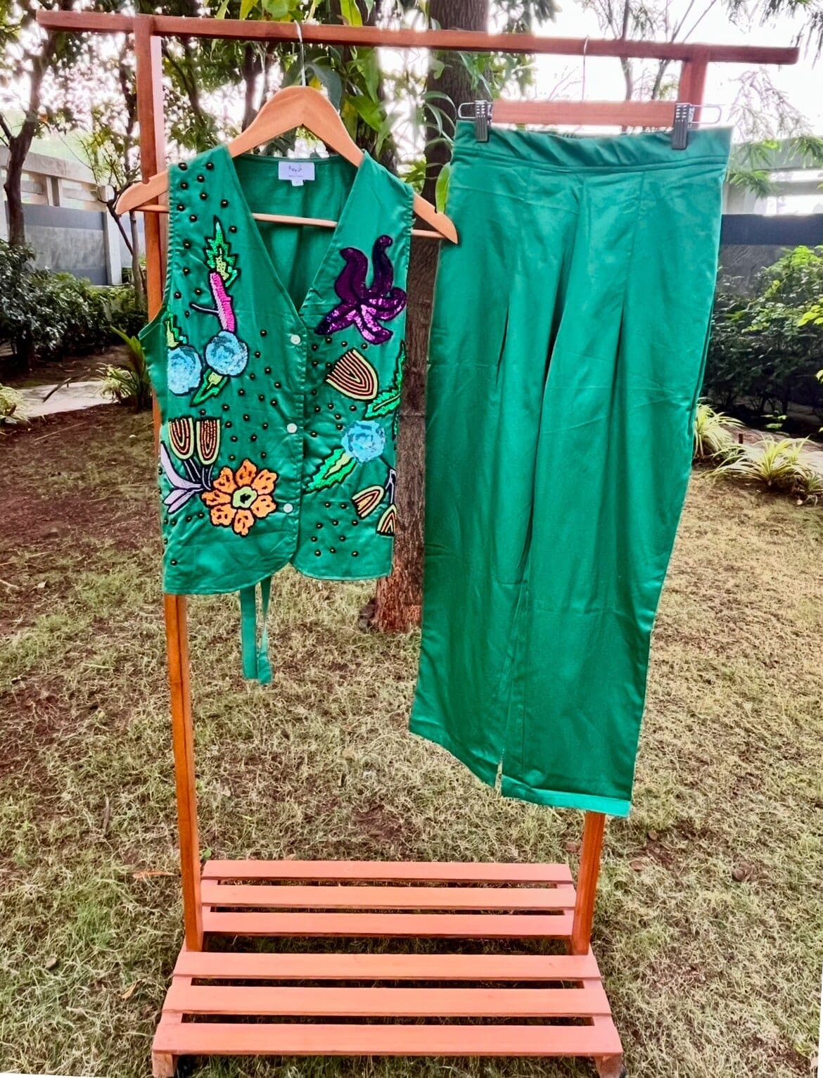 Vest and trousers on a wooden garden rail: sequin flowers and dark beads across the front, back tie hanging loose.