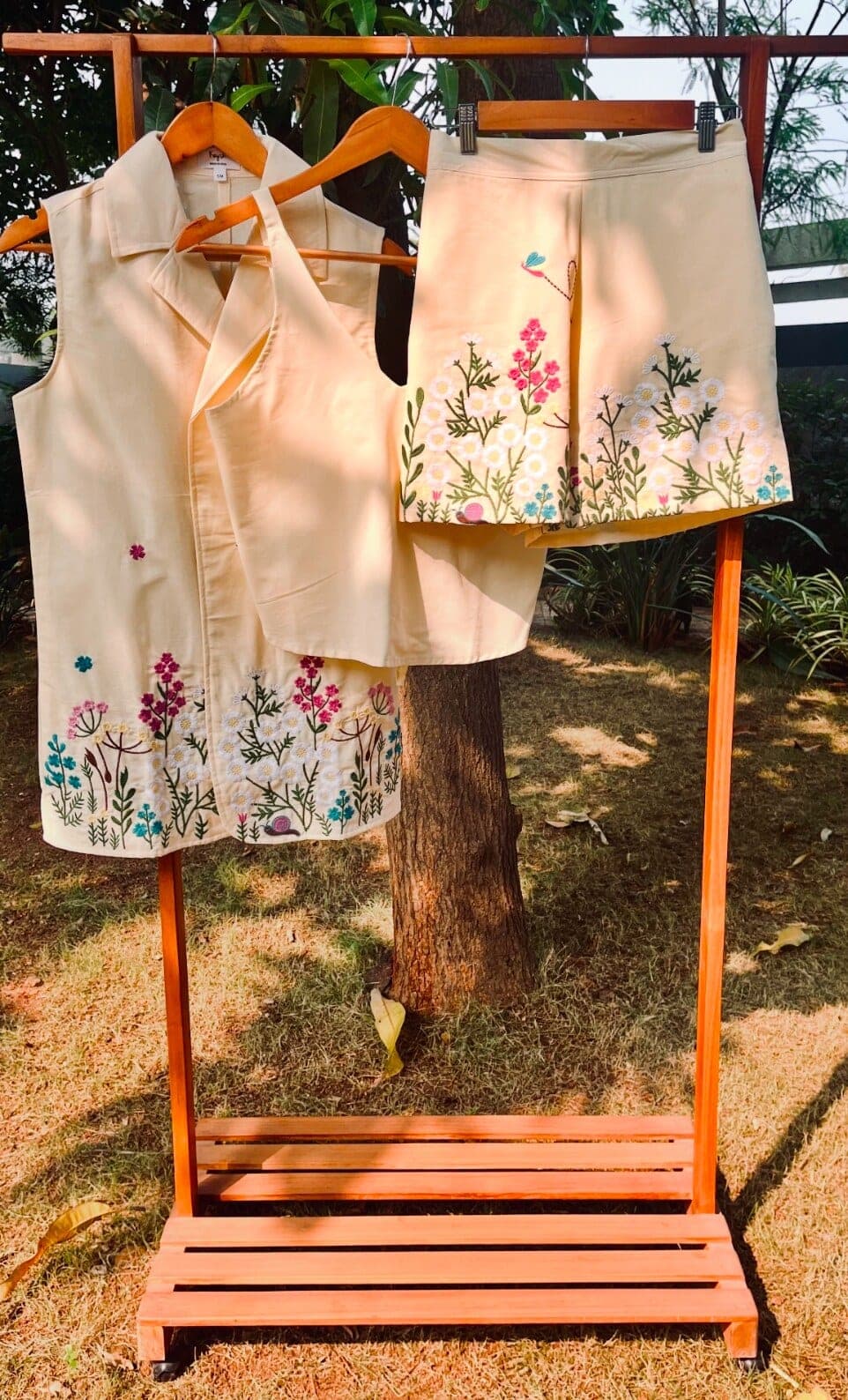 Cream cotton blazer set on a wooden rack — sleeveless jacket, camisole and shorts, wildflowers embroidered along every hem.