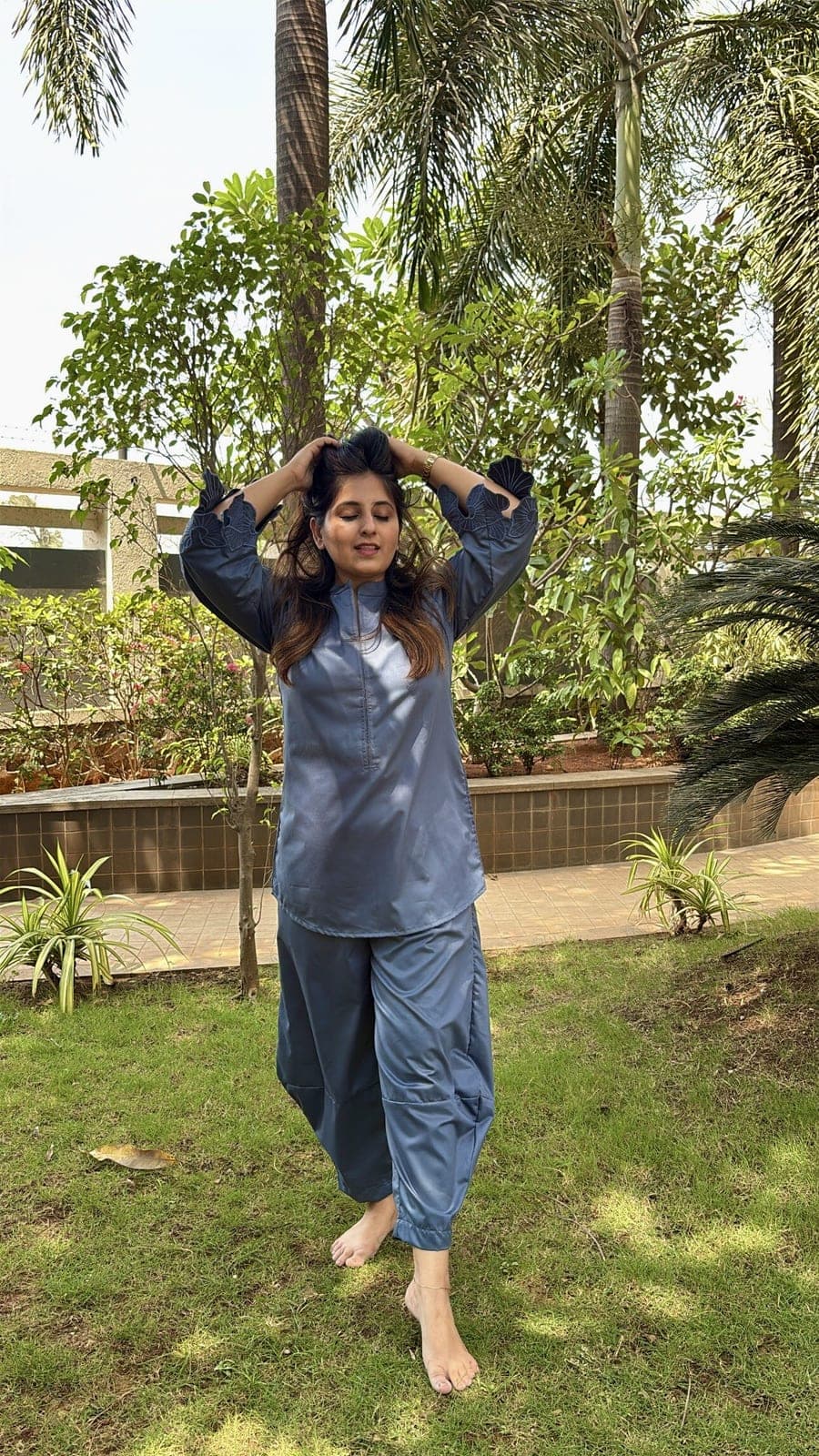 Steel blue viscose-blend co-ord photographed on grass, matching kurta and cuffed trousers, tone-on-tone cutwork opening at each sleeve end.
