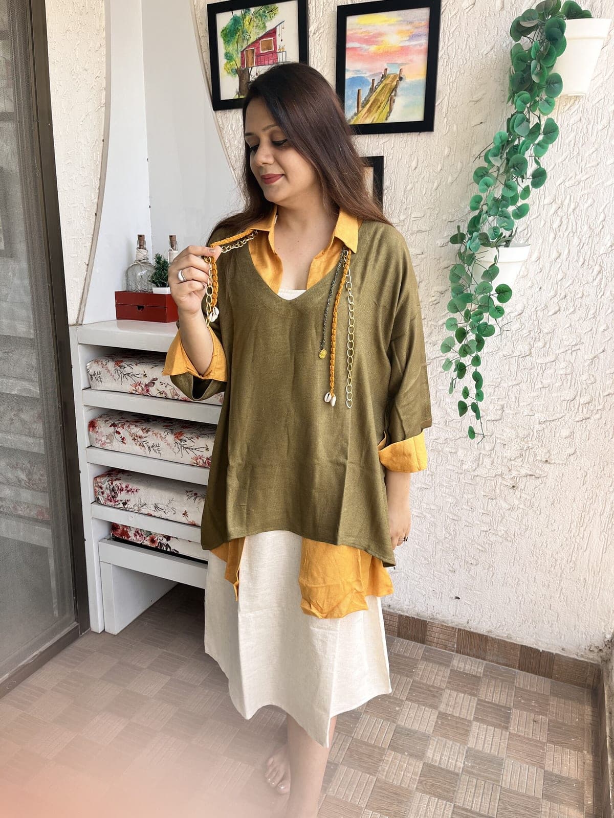 Olive green tunic with a mustard shirt beneath and the ivory slip below, a braided shell-tipped neck tie held up.