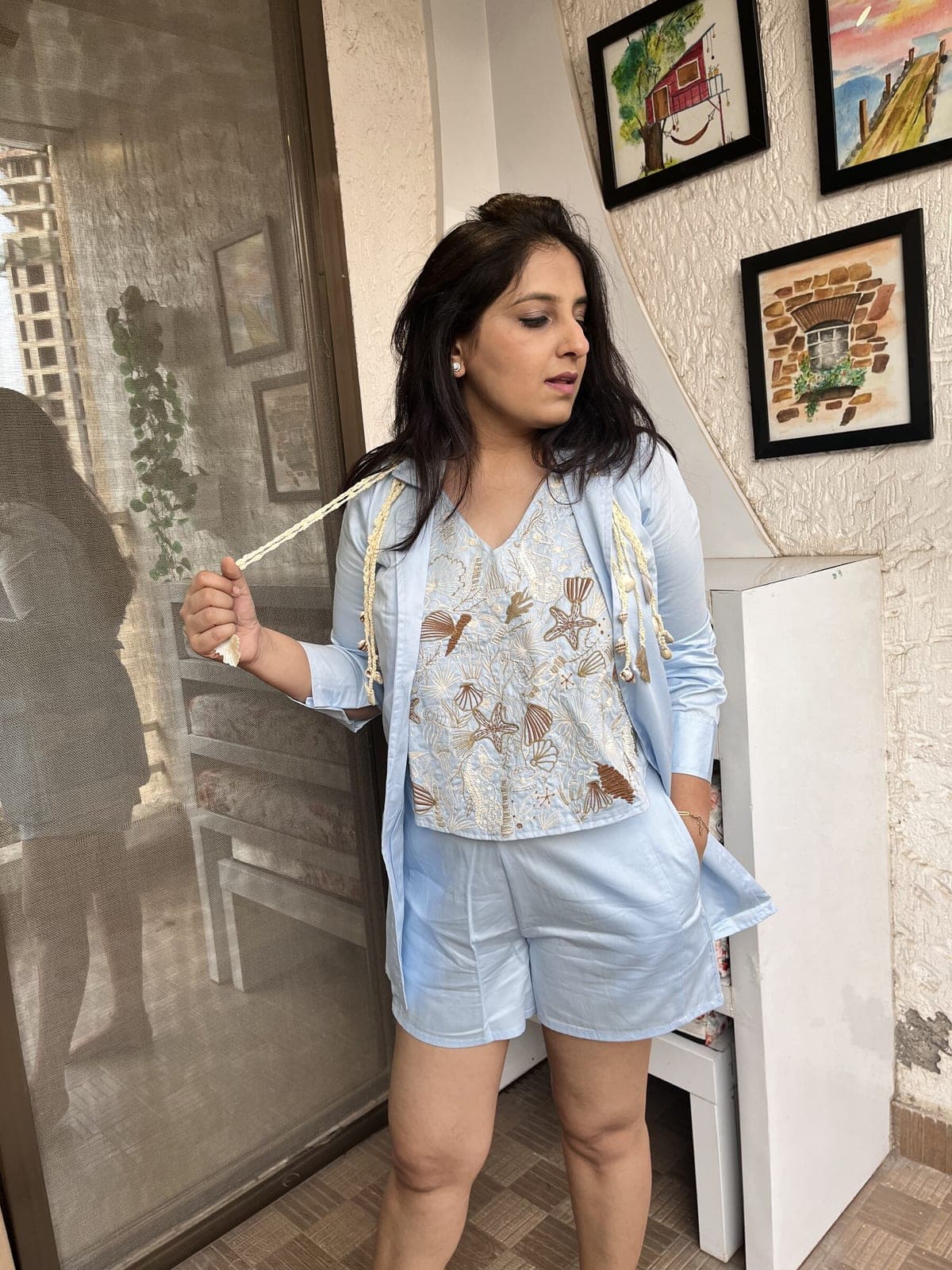 Powder blue cotton blazer worn open over a shell-and-starfish embroidered V-neck top and matching shorts, cream tassel cords at the lapels.