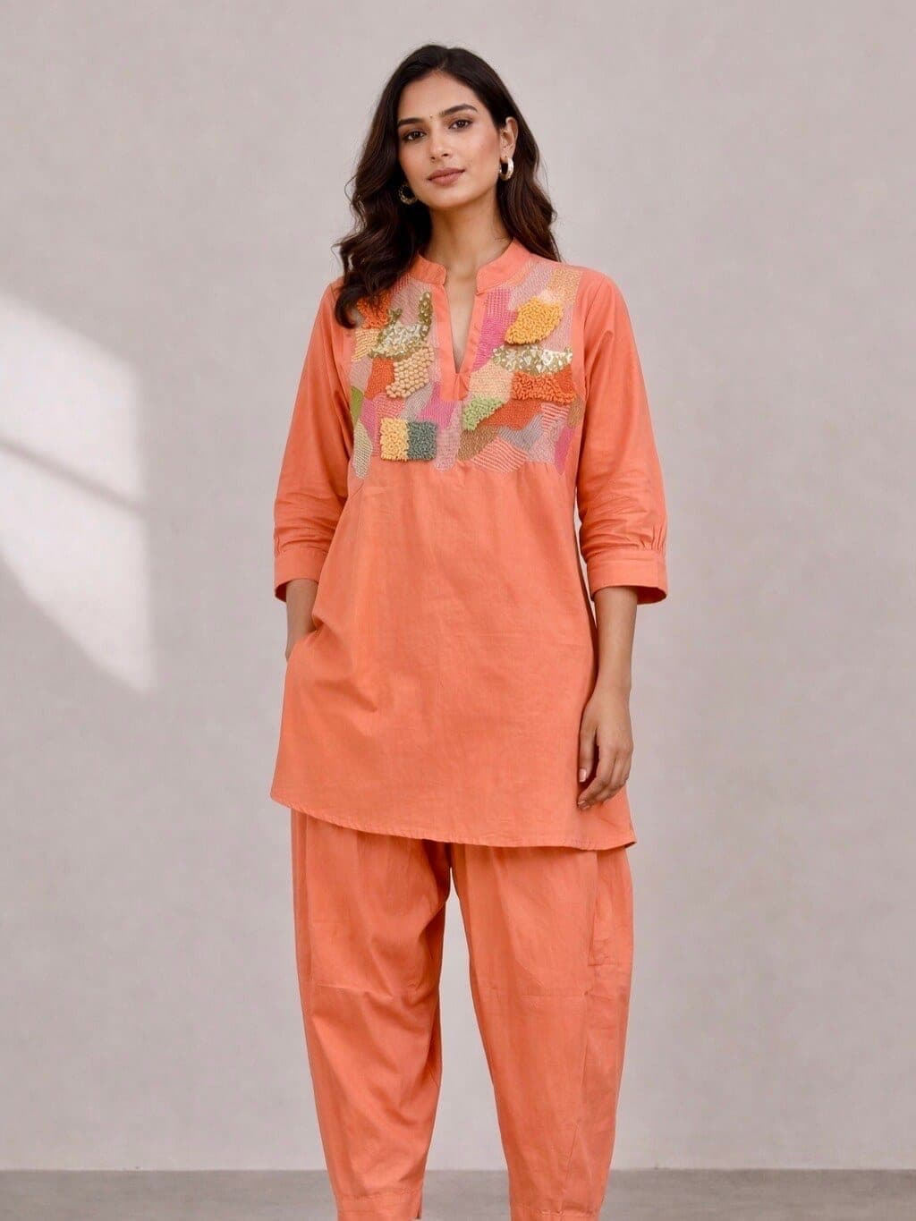 Coral cotton kurta with a multicoloured patchwork yoke, band collar and three-quarter sleeves, over matching pleated trousers that narrow at the ankle.