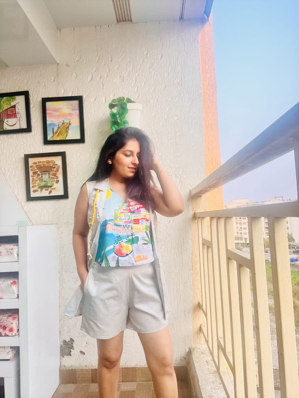 Sleeveless light grey blazer worn open over the printed Positano-scene top and matching pleated shorts, yellow beaded tassel at the lapel.