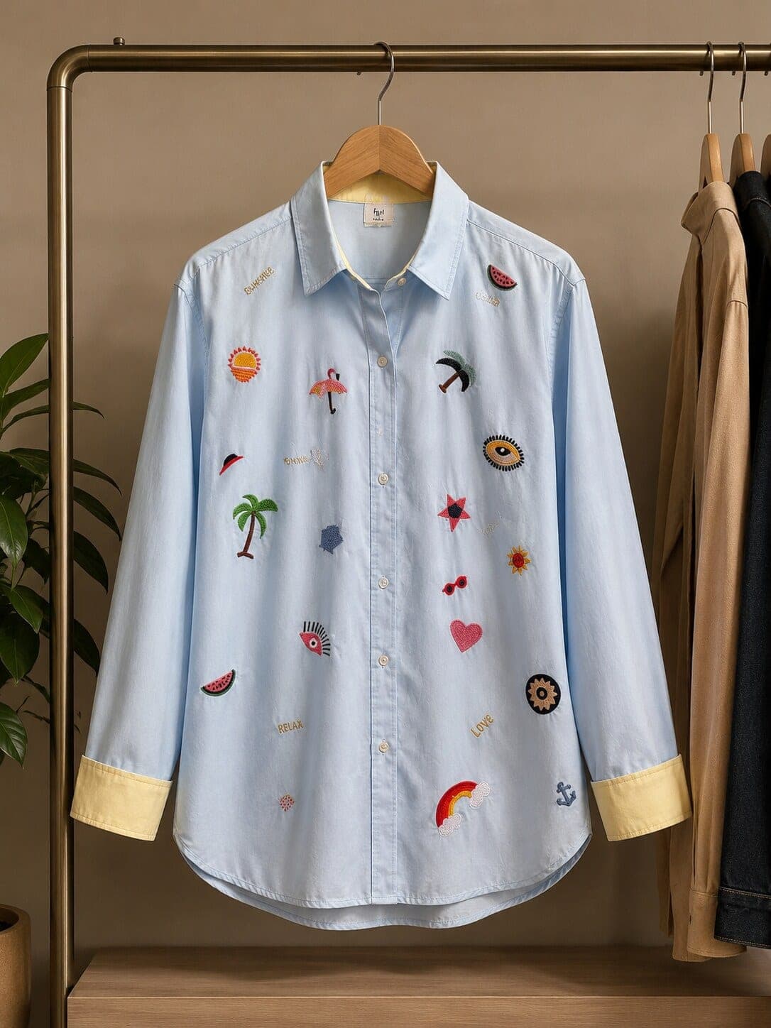 Hung on a brass rail, the powder blue cotton shirt shows its yellow contrast cuffs and scattered summer motifs.