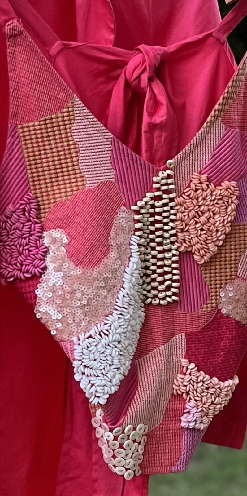 Close view of the patchwork panel — rose, apricot and coral patches under rice beads, sequins and white shells, a knotted tie above.