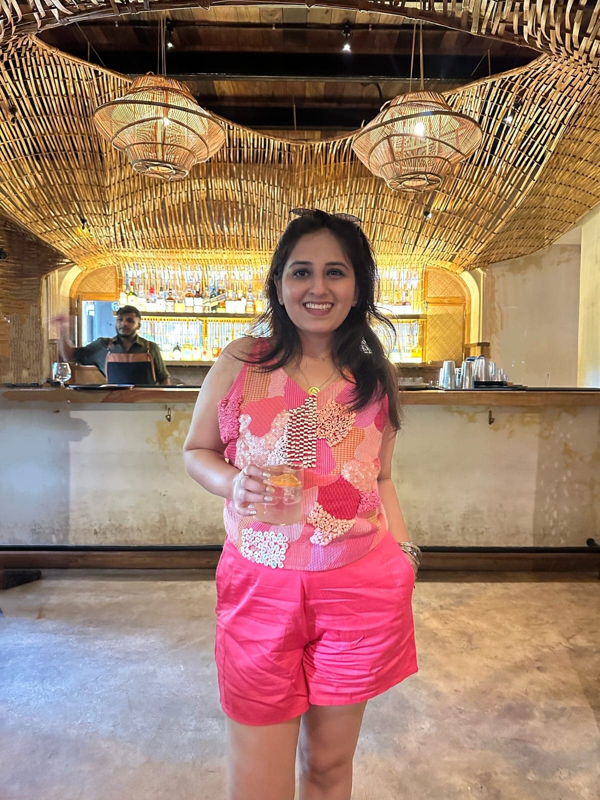 The sleeveless patchwork top worn on its own with pink shorts, photographed indoors against a bar counter.