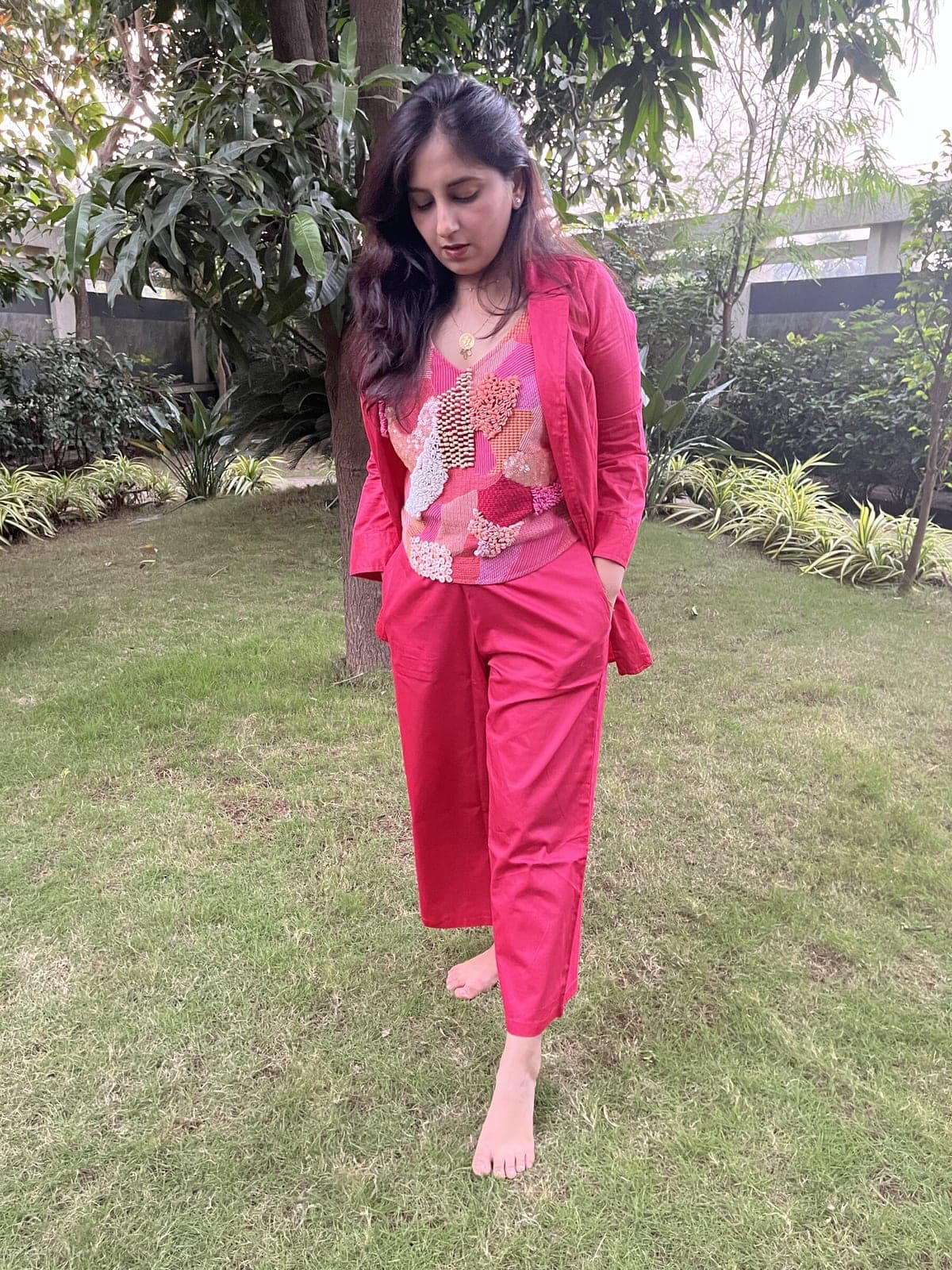 Deep pink blazer left open over the beaded patchwork top, here with matching straight-cut pink trousers, on grass.