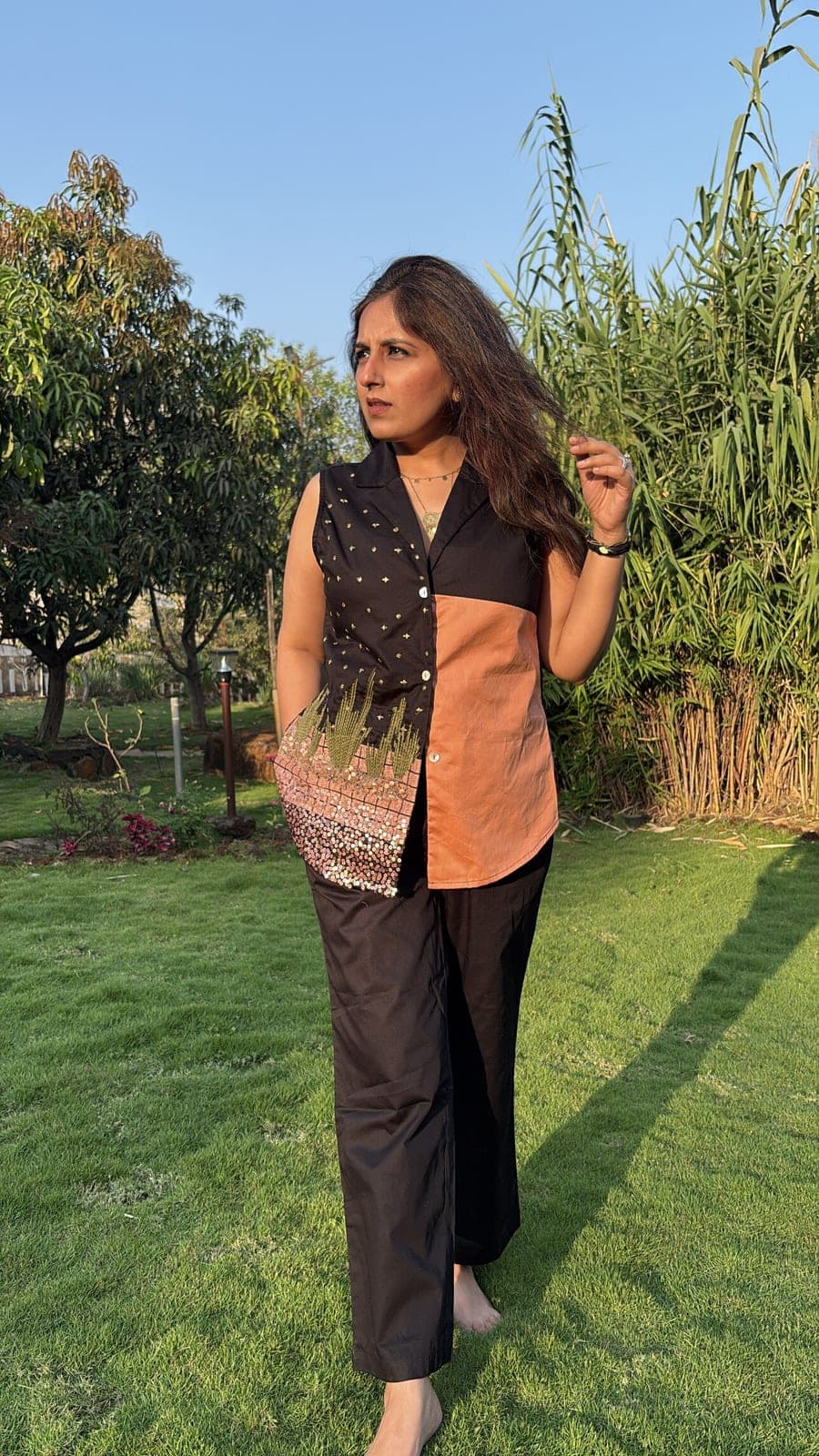 Full-length view with wide-leg black pants, terracotta panel beside the button placket, notched collar and curved hem just past the hip.