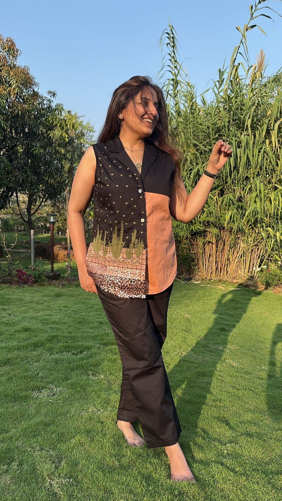 Three-quarter view in the garden showing the button placket, scattered gold stars and the rose-gold sequin band above the curved hem.