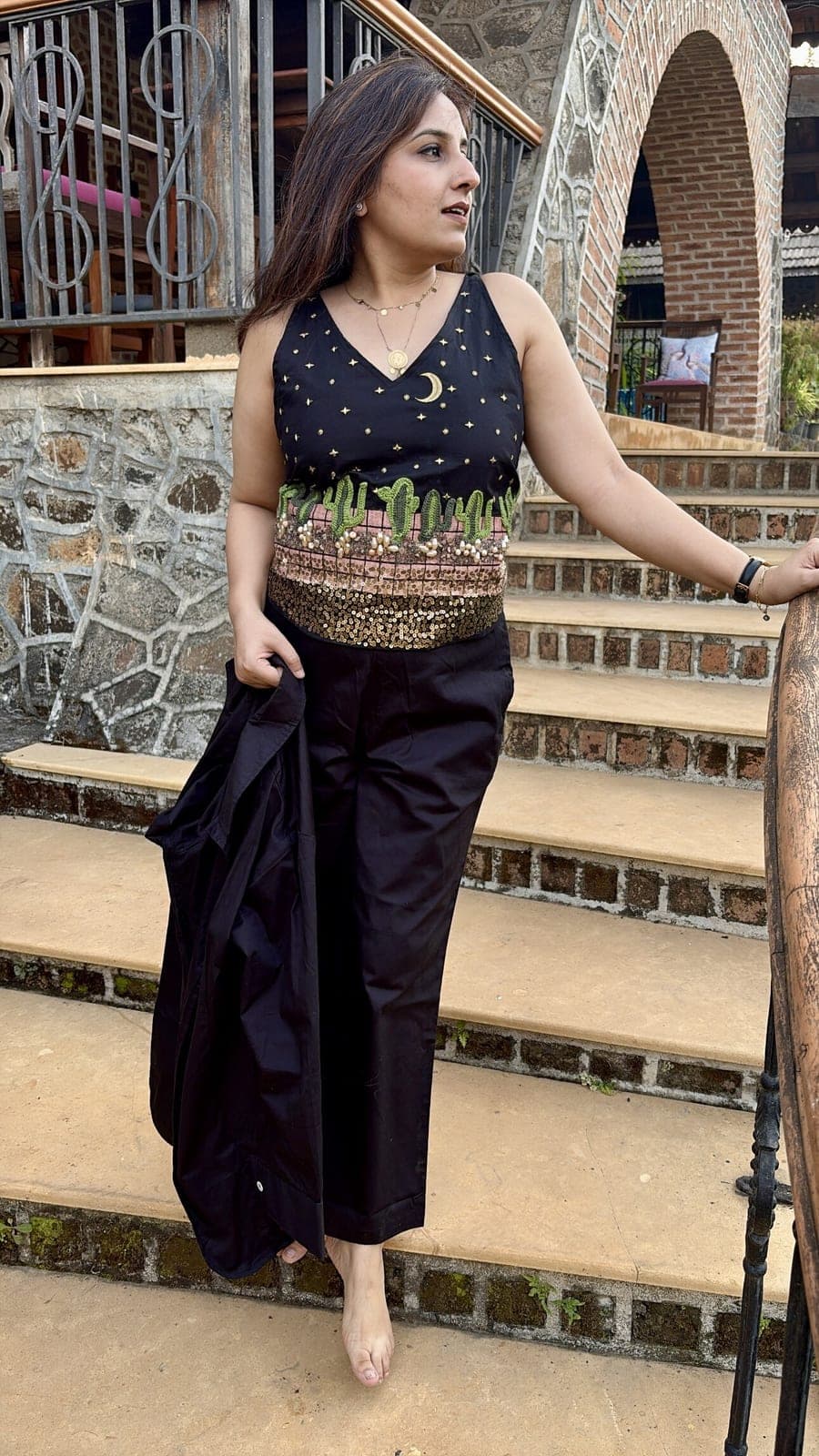 Blazer held in one hand on brick garden steps, leaving the sleeveless top's V-neck, scattered gold stars and waist sequin band visible.