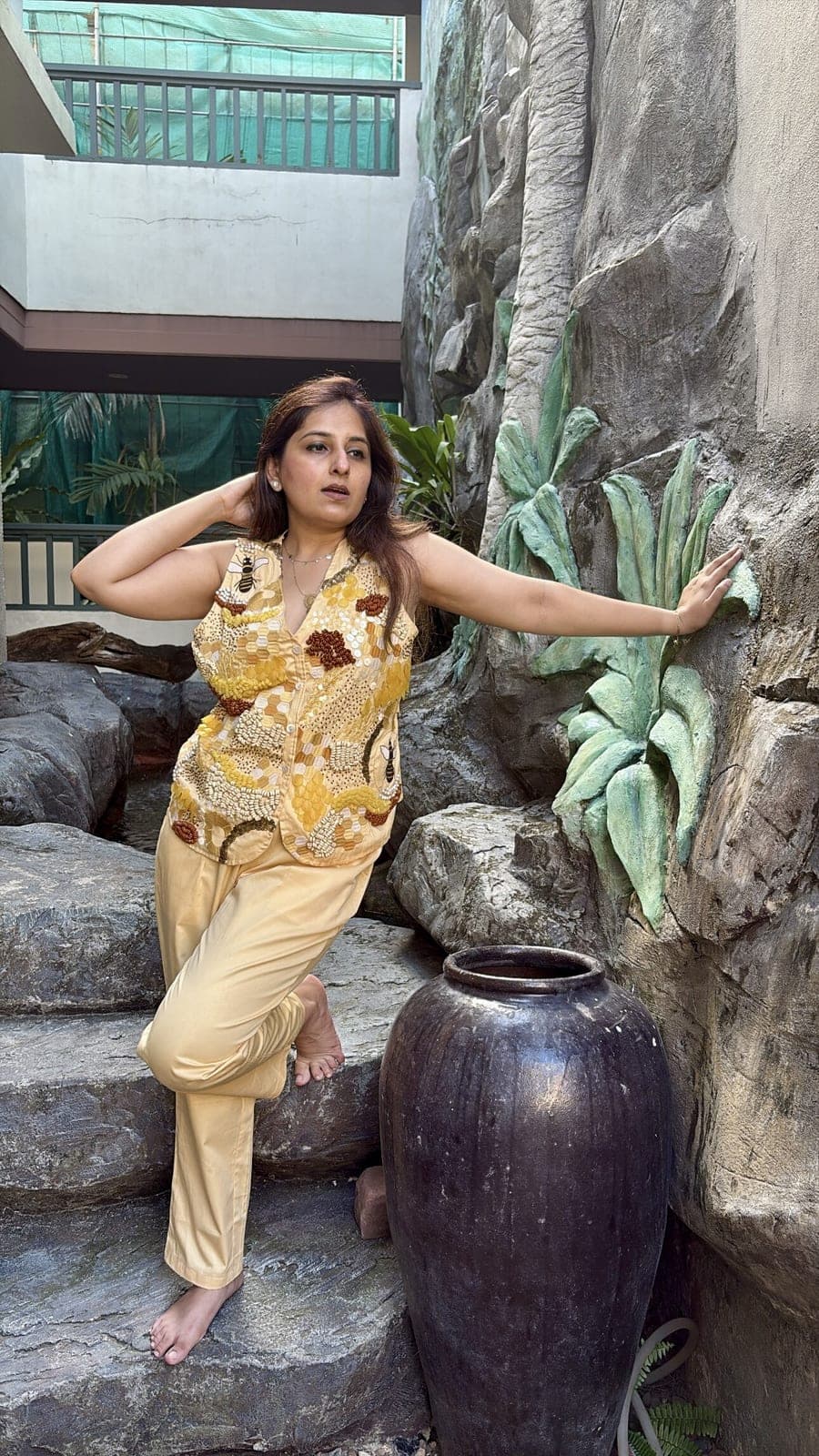 Model on stone steps in the yellow cotton co-ord: sleeveless beaded honeycomb top with an open collar over pale yellow straight pants.
