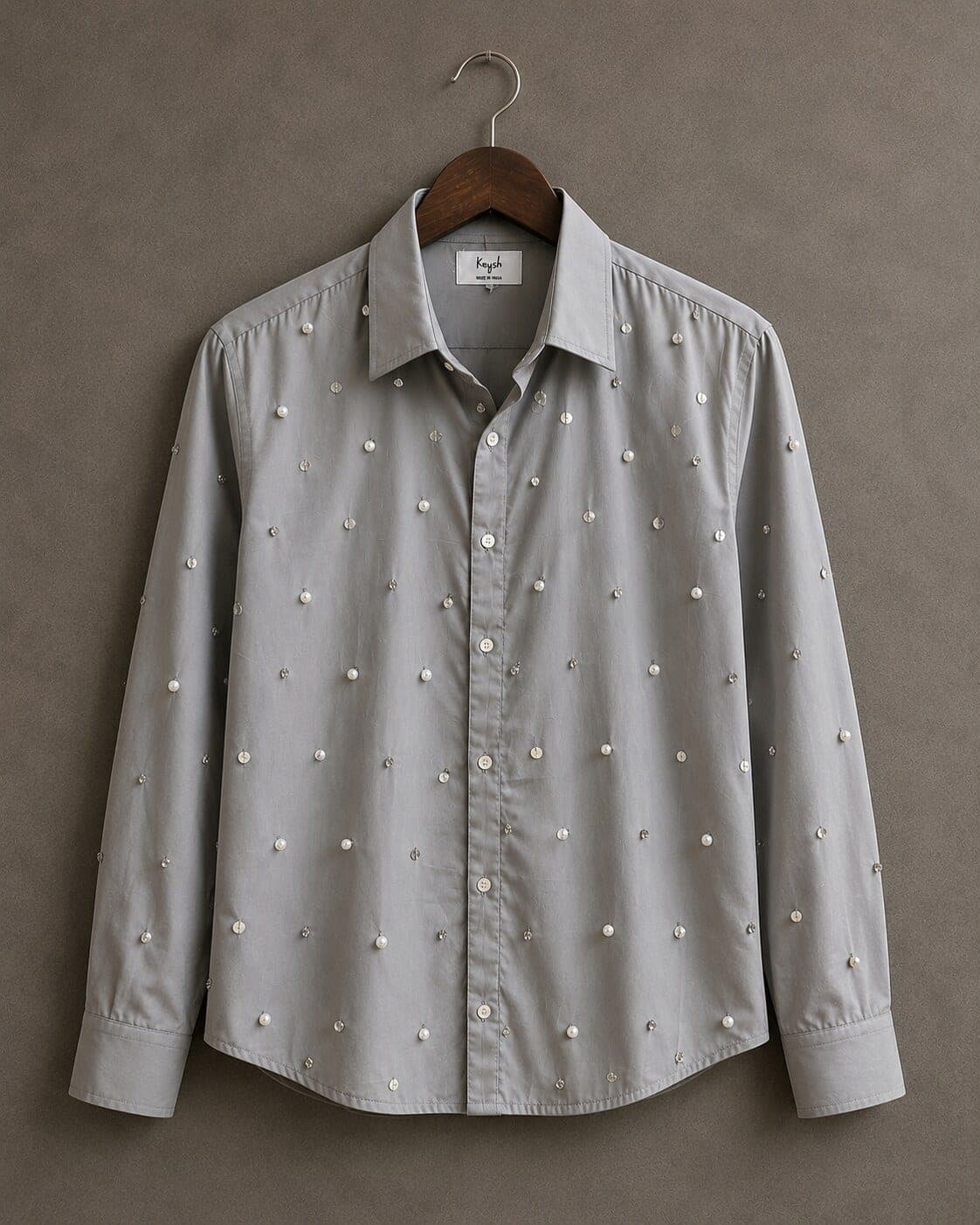 Grey cotton shirt on a wooden hanger, pearls and clear stones scattered evenly across the body, yoke and sleeves.